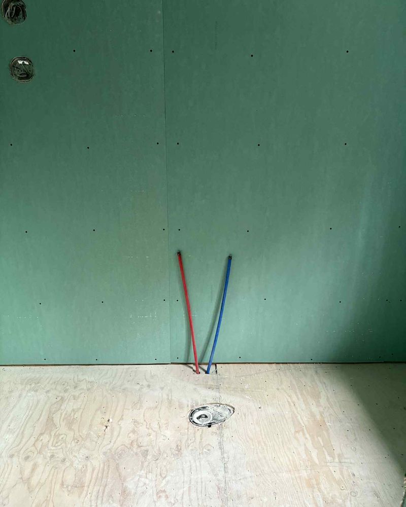 Green board wall, red and blue supply lines, toilet flange in the floor.