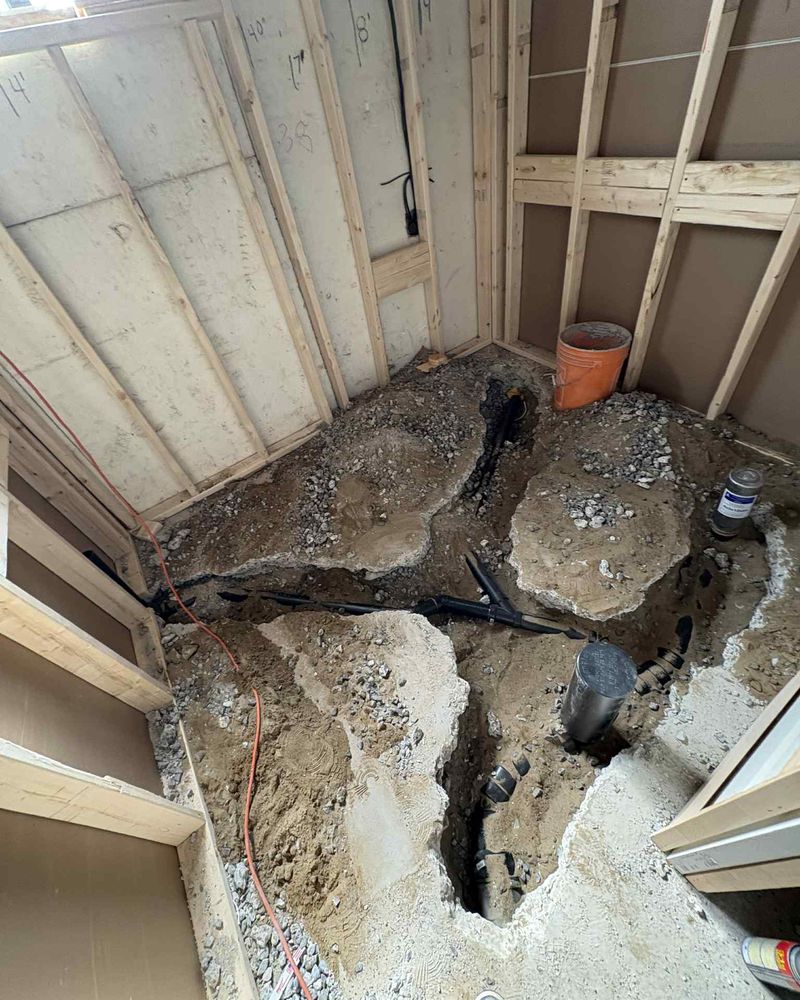Open trench in a basement slab, black drain pipe laid at the bottom.